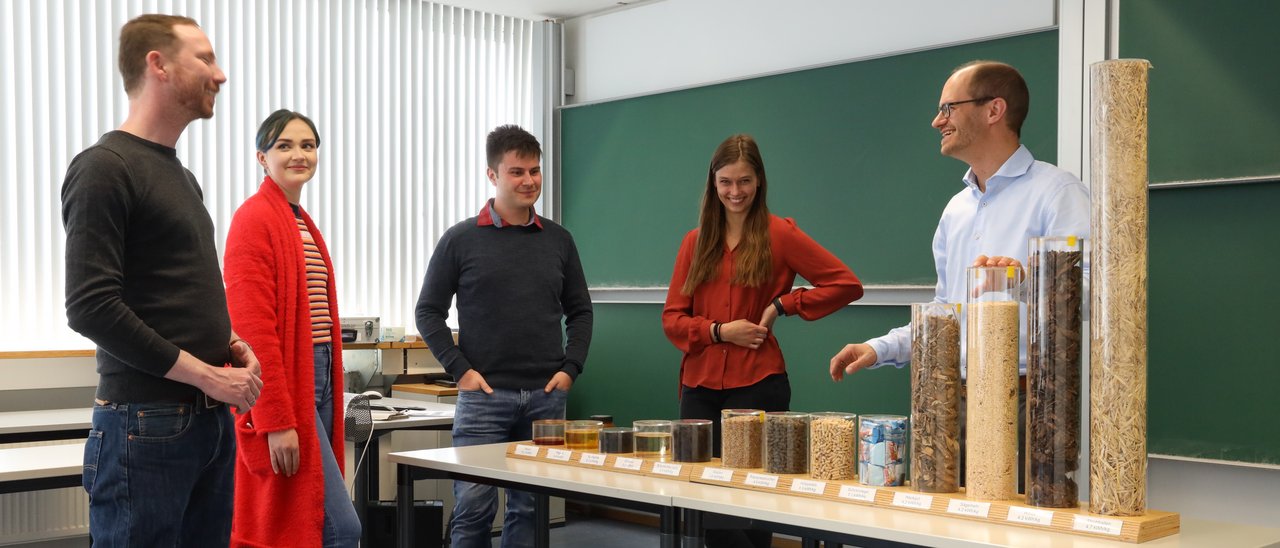 Der Professor zeigt einer Gruppe von Studenten verschiedene Materialien, um die Wattstunden pro Kilogramm darzustellen, die aus jedem Material gewonnen werden können