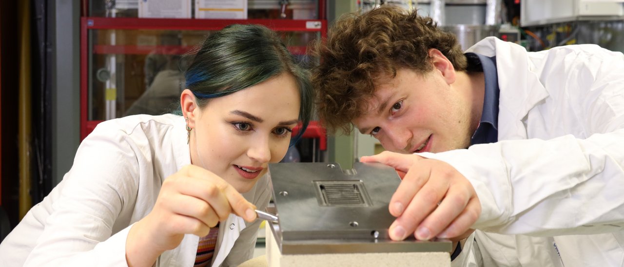 Zwei Studierende arbeiten in einem Labor zusammen an einer Vorrichtung 